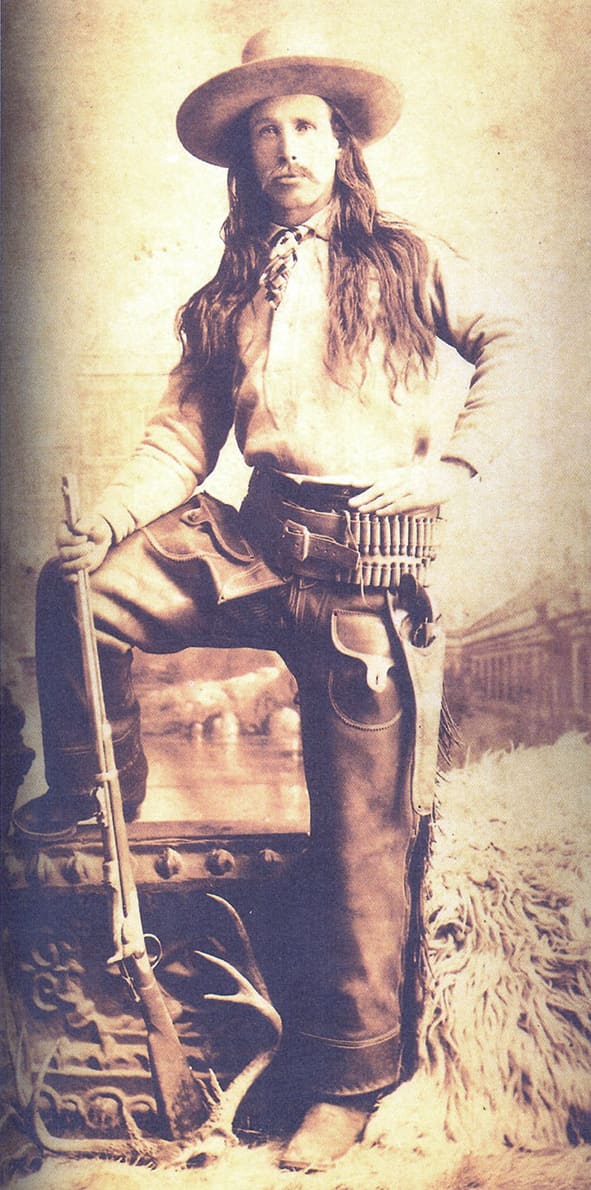 Studio portrait of Sheriff Commodore Perry Owens with rifle, long hair, and cartridge belt